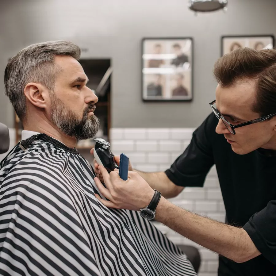 A barber trimming a customer beard in his shop